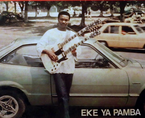 Pépé Félix Manuaku avec une guitare à double mache, appuyé contre une voiture grise