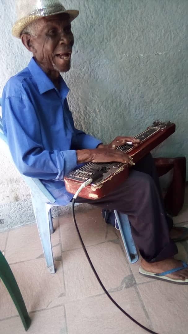 Roger Lokumu avec une guitare hawaïenne sur les genoux avec un chapeau